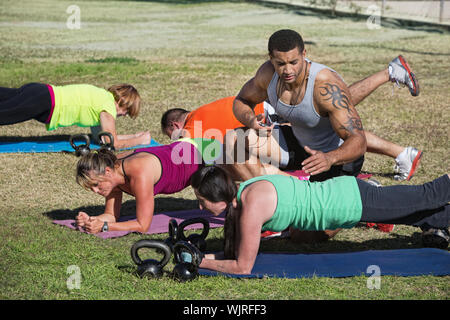 Muscular instructor with stopwatch helping students in fitness class Stock Photo