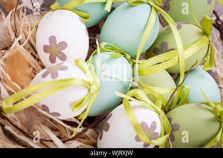 Collection of four hand decorated colourful green Easter eggs with different patterns displayed in straw, close up view Stock Photo