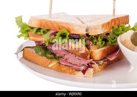 Delicious thinly sliced beef pastrami club sandwich with fresh curly lettuce served with a small dish of pickled vegetables on a white plate, isolated Stock Photo