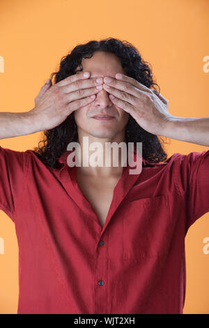 Handsome curly haired man covering his eyes with his hands Stock Photo