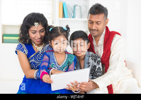 Indian Asian family using tablet pc computer at home. India family living lifestyle in traditional dress. Happy smiling parents and children. Stock Photo