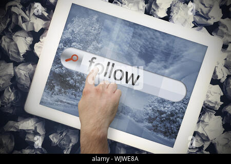 Hand touching the word follow on search bar on tablet screen on crumpled papers Stock Photo