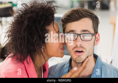 Closeup of a casual female artist whispering into colleagues ear at a bright office Stock Photo