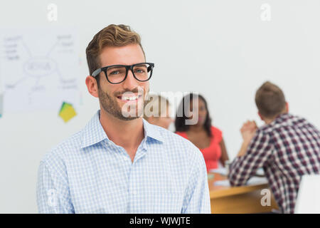 Handsome designer smiling at camera with colleagues behind him in creative office Stock Photo