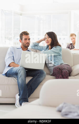 Focused designers working together on laptop on the couch in creative office Stock Photo