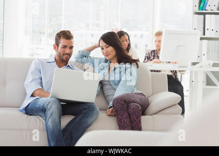 Young smiling designers working on laptop on the couch in creative office Stock Photo