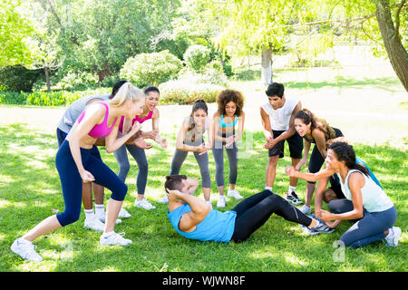 Group of friends cheering man doing sit ups in the park Stock Photo