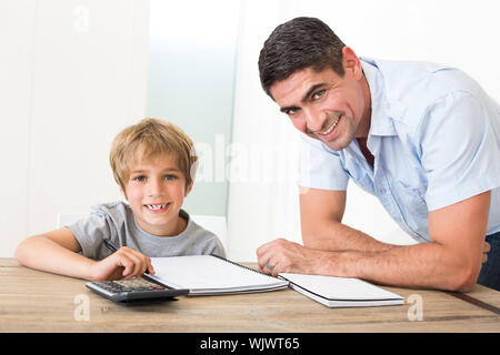 Portrait of happy father assisting son with homework at table in house Stock Photo