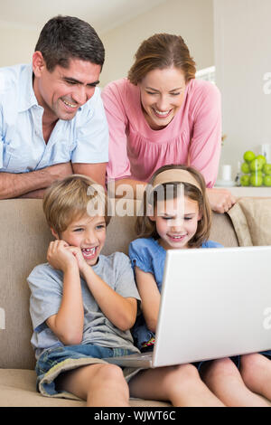 Happy parents watching children using laptop in living room Stock Photo