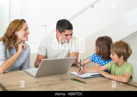 Parents with laptop assisting children coloring at table in house Stock Photo