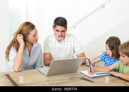 Parents using laptop while children coloring at table in house Stock Photo