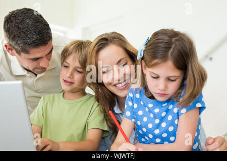 Father with son using laptop while mother and daughter coloring at home Stock Photo