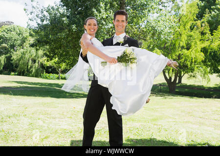 Portrait of happy young groom lifting bride in arms at garden Stock Photo