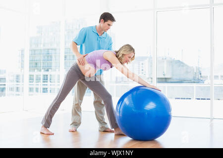 Trainer exercising with blonde pregnant client and exercise ball in a studio Stock Photo