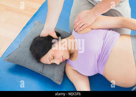 Masseur moving pregnant womans neck and shoulder in a fitness studio Stock Photo