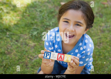 High angle portrait of a happy young girl holding block alphabets as 'play' at the park Stock Photo