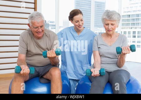 Female therapist assisting senior couple with dumbbells in the medical office Stock Photo