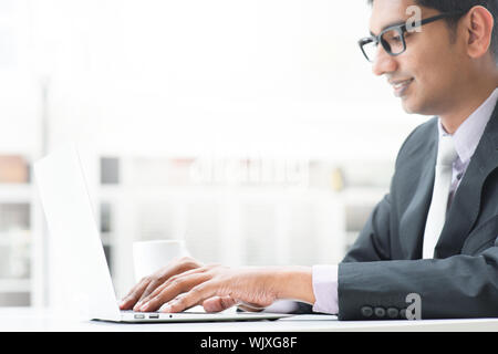 Young Asian Indian businessman using a  laptop  or notebook computer during office break at cafe, relaxing with a cup of coffee. India male business m Stock Photo