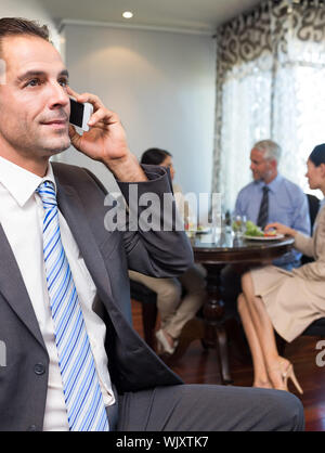 Businessman using cellphone with colleagues having meal in background at the table Stock Photo