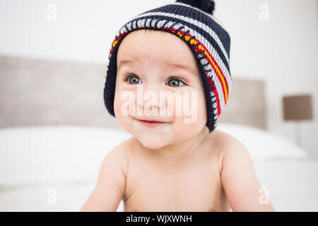 Smiling baby boy wearing knit hat looking away in bedroom Stock Photo