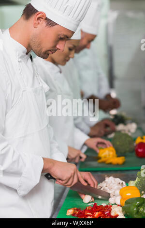 Row of trainee chefs slicing vegetables in a commercial kitchen Stock Photo