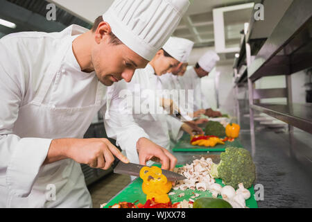 Row of trainee chefs slicing vegetables in a commercial kitchen Stock Photo