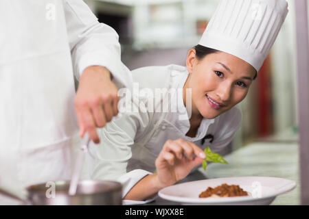 Happy chef putting basil leaf on spaghetti dish in a commercial kitchen Stock Photo