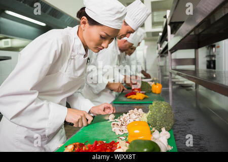 Row of trainee chefs slicing vegetables in a commercial kitchen Stock Photo
