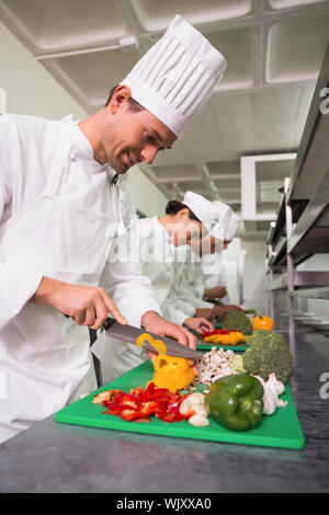 Row of trainee chefs slicing vegetables in a commercial kitchen Stock Photo