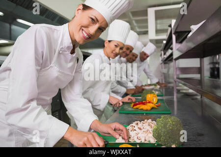 Row of happy trainee chefs slicing vegetables in a commercial kitchen Stock Photo