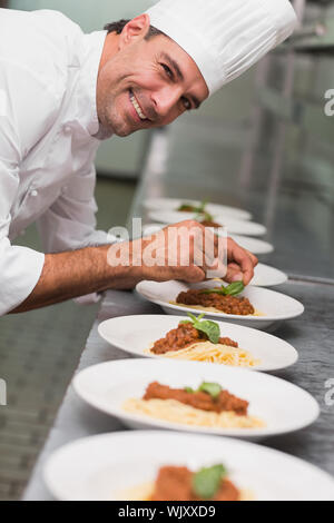 Happy chef putting basil leaf on spaghetti dish in a commercial kitchen Stock Photo