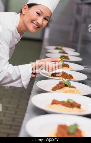 Happy chef putting basil leaf on spaghetti dish in a commercial kitchen Stock Photo