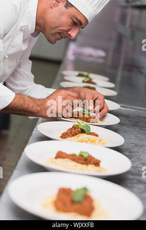 Happy chef putting basil leaf on spaghetti dish in a commercial kitchen Stock Photo