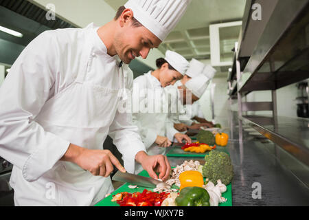 Row of trainee chefs slicing vegetables in a commercial kitchen Stock Photo