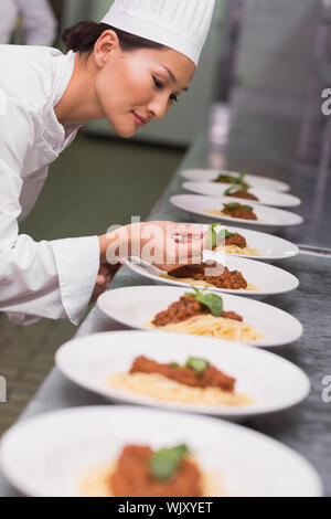 Happy chef putting basil leaf on spaghetti dish in a commercial kitchen Stock Photo