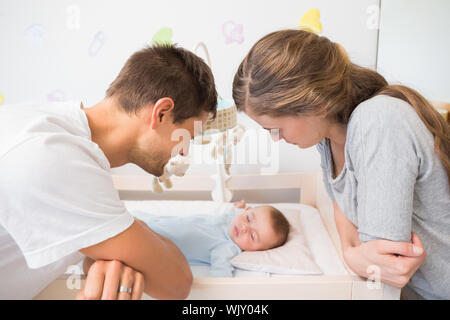 Happy parents watching over baby son in crib at home in bedroom Stock Photo