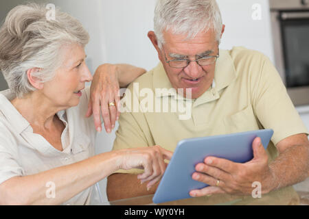 Happy senior couple using tablet pc at the table at home in the kitchen Stock Photo