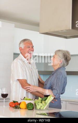 Happy senior couple hugging while preparing a meal at home in the kitchen Stock Photo