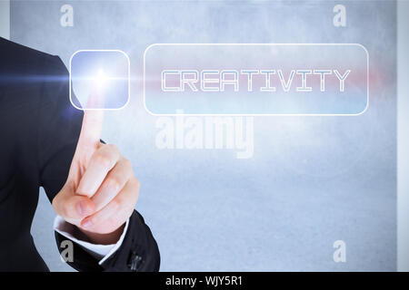 Businesswomans finger touching creativity button against grey wall Stock Photo