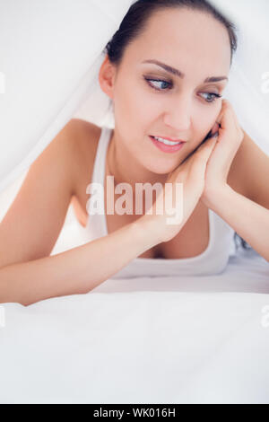 Happy brunette lying under the sheets looking away Stock Photo