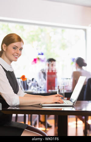 Attractive businesswoman working on laptop smiling at camera Stock Photo