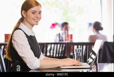 Smiling businesswoman working on laptop looking at camera Stock Photo