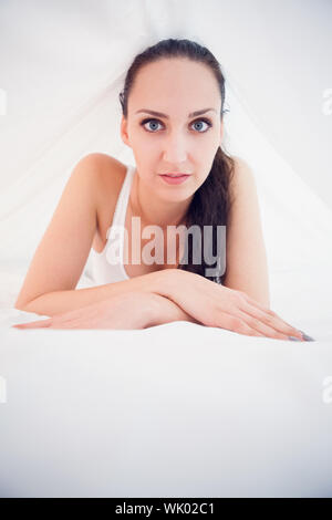 Pretty brunette lying under the sheets smiling at camera Stock Photo