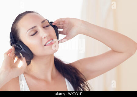 Relaxed brunette sitting on bed listening to music Stock Photo