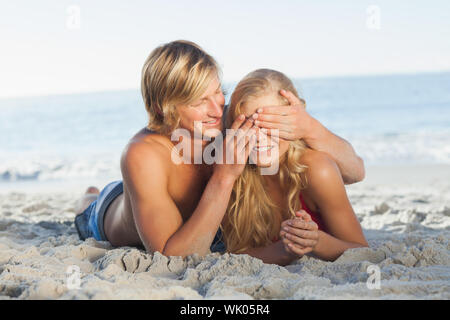 Man covering girlfriends eyes lying on the beach Stock Photo