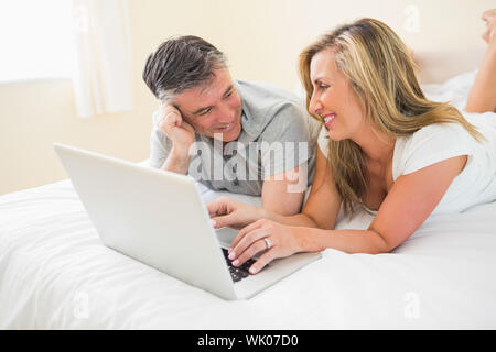 Laughing couple lying on bed using a laptop Stock Photo