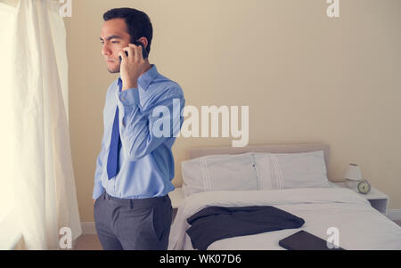 Stressed man calling someone with a mobile phone and looking out the window Stock Photo
