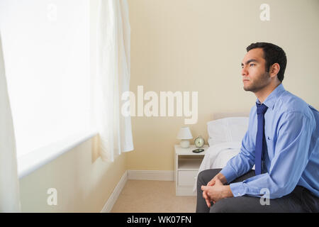 Unsmiling man looking out the window sitting on his bed Stock Photo
