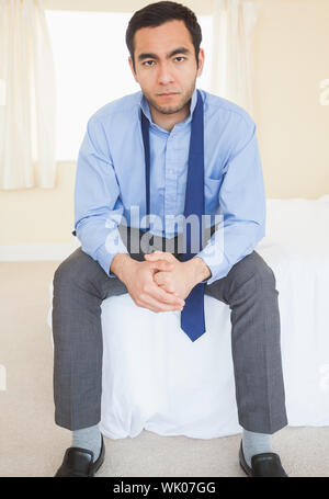 Unsmiling man sitting on his bed Stock Photo