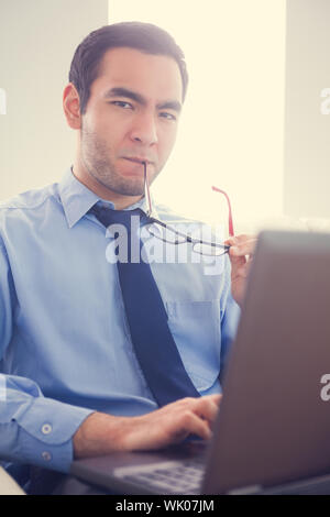 Irritated man biting his eyeglasses and using a laptop Stock Photo